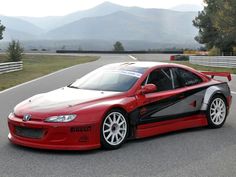 a red and black sports car driving on a race track with mountains in the background