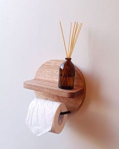 a wooden shelf holding two rolls of toilet paper and a brown bottle with reeds in it