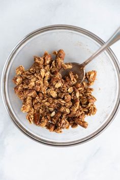 a glass bowl filled with granola on top of a white counter next to a spoon