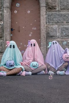 three people dressed as ghost sitting on the ground in front of a door with soap bubbles floating around them