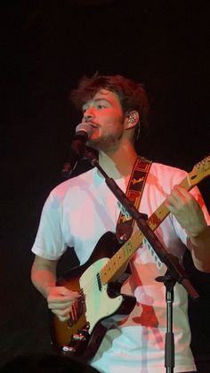 a man that is standing up with a guitar in his hand and singing into a microphone