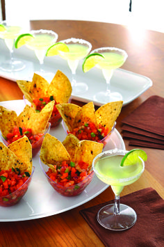 small cups filled with salsa and tortilla chips on a plate next to a margarita