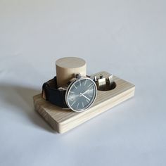 a watch sitting on top of a wooden stand next to an earbud holder