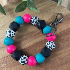 a colorful bracelet with black, pink, and blue beads on a wooden table next to a potted plant