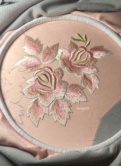 there is a pink flower embroidered on the side of a round object with silver trim