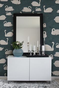 a white cabinet sitting in front of a mirror on top of a dresser next to a wall