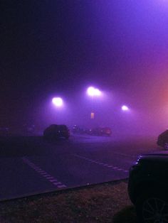 cars driving on a foggy road in the middle of an empty parking lot at night