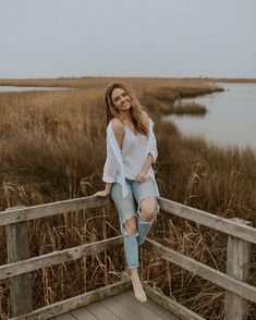 a woman is sitting on a wooden bridge in front of some tall grass and water