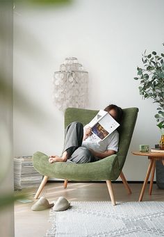 a person sitting in a green chair reading a book while wearing slippers and holding a magazine