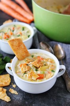 two bowls of soup with crackers and carrots next to it on a table