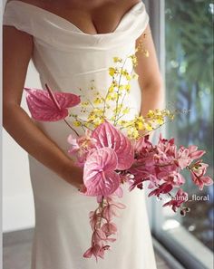 a woman in a white dress holding a bouquet of pink and yellow flowers on her arm