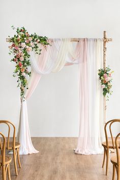 a white and pink wedding arch decorated with flowers, greenery and draping