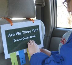 a child in the back seat of a car playing with a sign that says are we there yet?