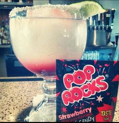 a drink in a tall glass with a lime slice on the rim next to a bag of pop rocks