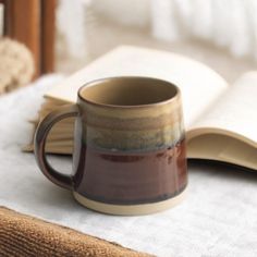 a coffee mug sitting on top of a bed next to an open book