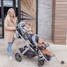 a woman standing next to a baby in a stroller with another child on it