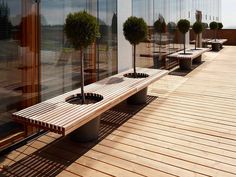 an empty bench sitting on top of a wooden deck next to tall buildings with glass windows