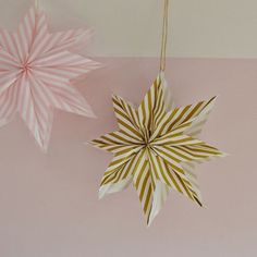 two paper snowflakes hanging from strings on a pink and white striped wallpaper