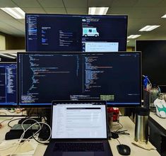 a laptop computer sitting on top of a desk in front of two large monitors with data