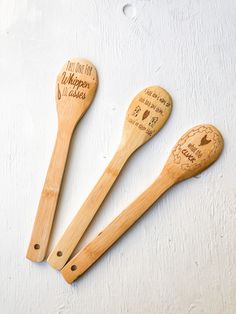 three wooden spoons with writing on them sitting next to each other, one is holding a spatula