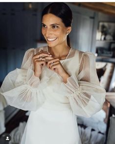 a woman in a white dress smiling at the camera with her hands on her chest