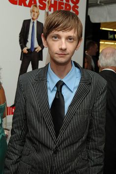 a man wearing a suit and tie standing in front of a poster