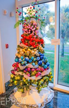 a colorful christmas tree with ornaments on it in front of a glass door and window