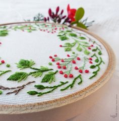 a close up of a embroidery on a wooden hoop with holly and red berries in the center