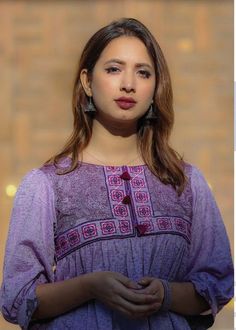 a woman in a purple dress is standing with her hands on her hips and looking at the camera