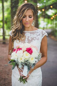 a woman in a wedding dress holding a bridal bouquet and looking down at the camera