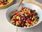 corn and black bean salad in a white bowl with a wooden spoon on the side