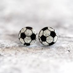 a pair of black and white soccer ball stud earrings with glitter on them sitting on a concrete surface