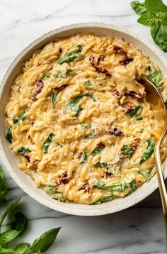 a white bowl filled with pasta and spinach on top of a table next to green leaves