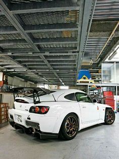 a white sports car parked in a garage under a metal structure with lots of shelves