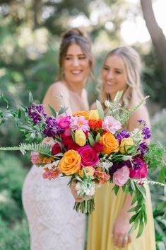 two bridesmaids holding colorful bouquets in their hands and smiling at the camera