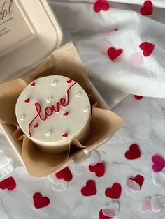 a cake with the word love on it in a box surrounded by red and white confetti