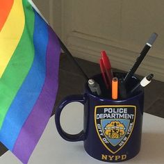 a police department mug with pens and pencils in it next to a rainbow flag