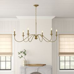 a chandelier hangs over a fireplace in a white living room with beige roman shades