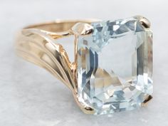 an aqua blue topazte ring is shown on a white surface with gold accents