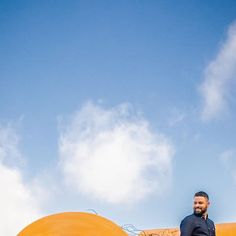 a man standing on top of a giant yellow object in the sky with clouds behind him