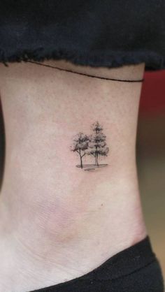 a small tree tattoo on the side of a woman's ankle, with trees in the background