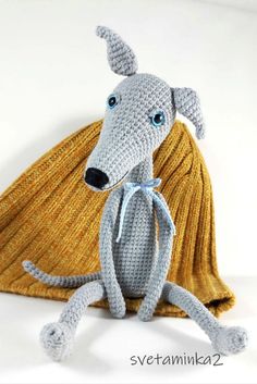 a crocheted gray dog sitting on top of a yellow blanket with blue eyes