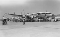 an old black and white photo of people standing in front of a plane on the tarmac