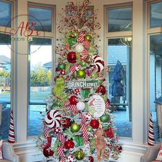 a christmas tree decorated with candy canes, ornaments and other holiday decorations in front of large windows