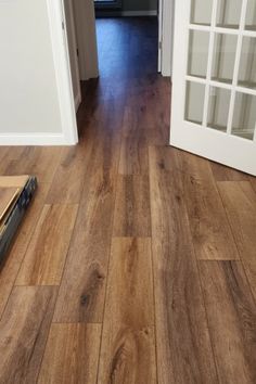 an open door leading to a hallway with hard wood flooring on the ground and white walls