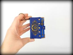 a hand holding a small blue book with gold trimmings and a keychain