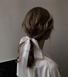 the back of a woman's head wearing a white blouse with a large bow