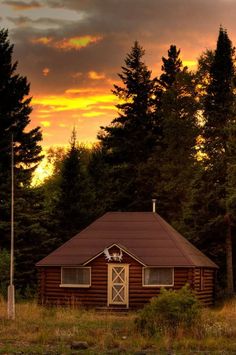 a small cabin sits in the middle of a field with trees around it at sunset