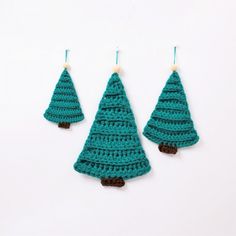 three crocheted christmas trees are hanging from hooks on a white surface, one is green and the other is brown