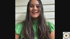 a woman with long hair wearing a green shirt and smiling at the camera while standing in front of a house